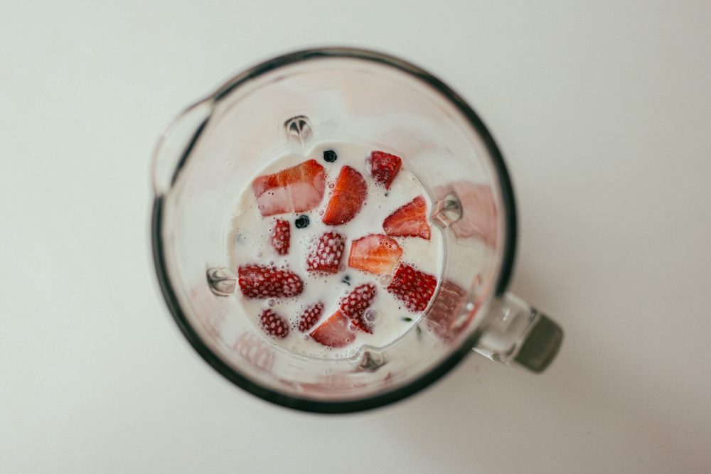 Overhead view of a glass blender jug with fresh strawberries and milk, part of our from-scratch prep.
